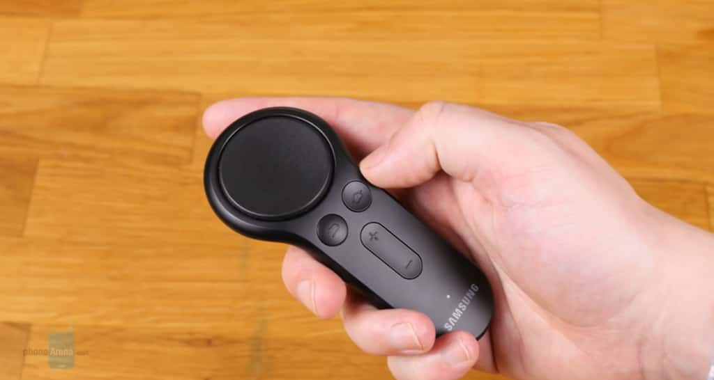 A hand holding a black, circular Samsung remote with buttons