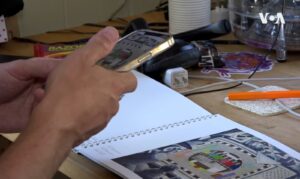 A person's hands with a mobile device scanning a piece of paper on a cluttered work table