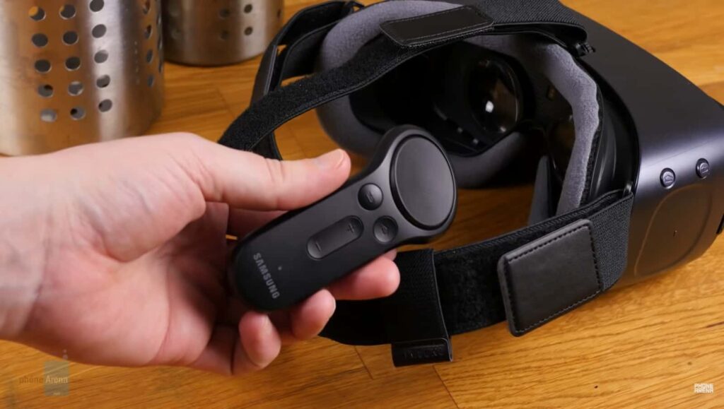 A Samsung VR controller in hand with its headset on a wooden surface